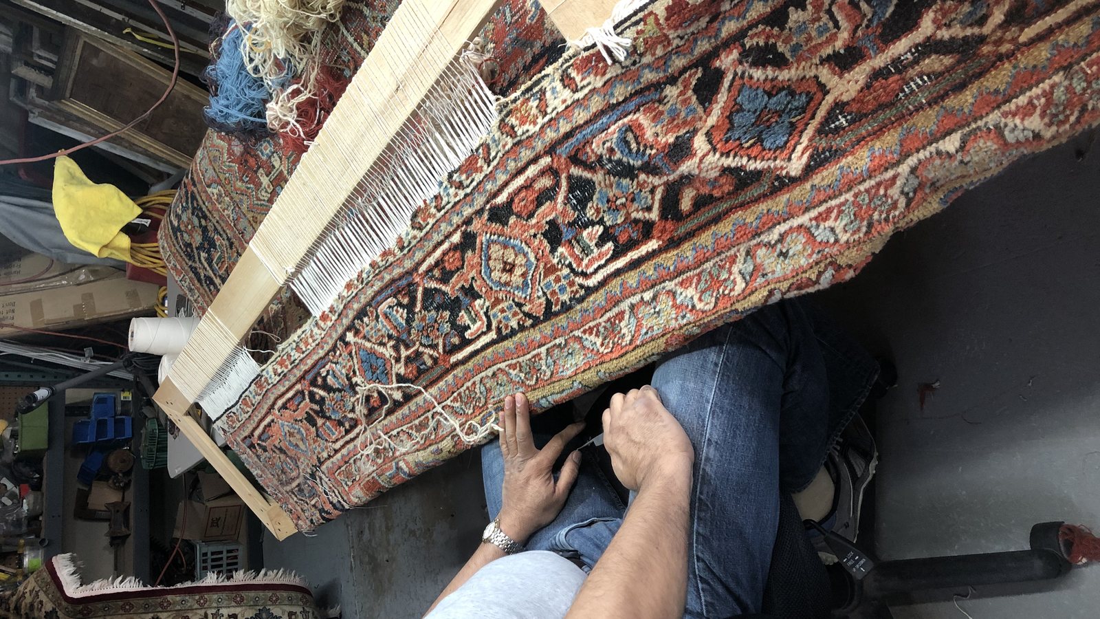 Hand re-knotting fringe on a loom frame clamped to the end of a rug