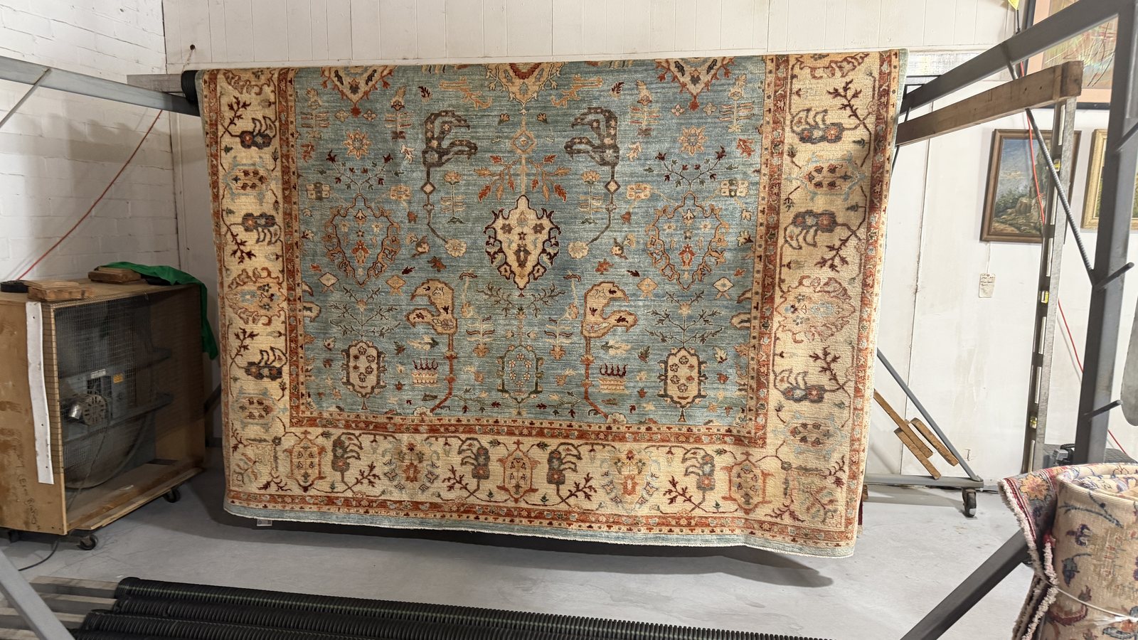 Pale blue and cream hand-knotted rug hanging over a drying rack